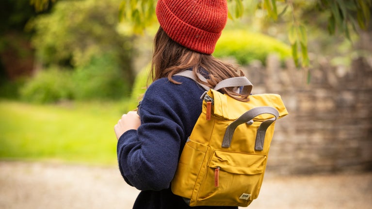 A woman wears a woolly hat and a yellow ROKA rucksack